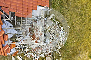 Aerial view on damaged red single house roof after strong wind or explosion. Hole in the rooftop and floor. Rubble on the ground