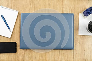 Aerial view of a desk with a closed laptop, a notepad, and a cell phone. Technology concept