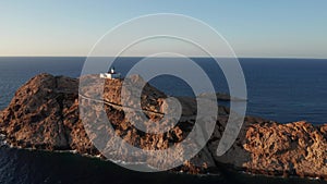 Aerial view of a desolated lighthouse in the middle of a desert island in the ocean, sea. Rocky shore and blue