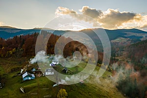 Aerial view of distant village with small shepherd houses on wide hill meadows between autumn forest trees in Ukrainian Carpathian
