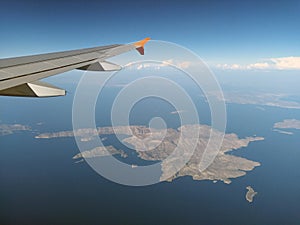 Aerial view of the dodecanese greek islands of kalymnos and telendos from an airplane with wing visible with blue sky and clouds o