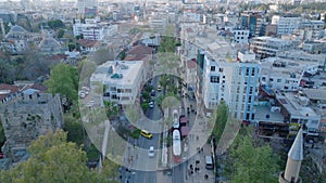 Aerial view of double car tram passing around buildings in city. Row of tall palm trees in tropical destination. Tilt up