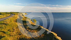 Aerial view of driving black car on the road along the cliff near the sea in summer at sunset.