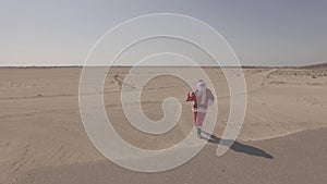 Aerial view, drone, air shoot. Santa Claus with sack walks on sand, found asphalt road in desert. Dlog profile. Comes
