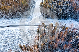 Aerial view from drone of car on curvy snow covered road in the winter forest