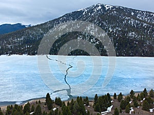 Aerial View from a Drone Flying above Frozen Lake Cracked Ice Mountains