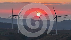 Aerial view drone orbit around silhouette wind turbines farm at sunset