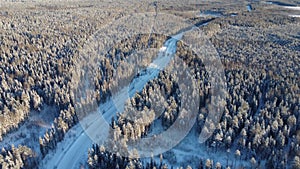Aerial view from a drone of a road in the middle of snow-covered trees and snow-covered forest on a winter day. A dense