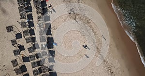 Aerial view, drone shot on the coast of Angola, people resting and playing on beach sand, surf boards on thatched huts