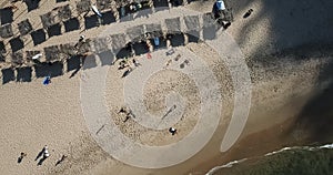 Aerial view, drone shot on the coast of Angola, people resting and playing on beach sand, surf boards on thatched huts