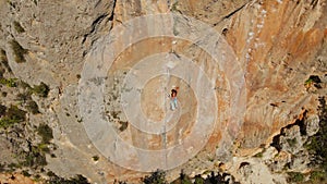 aerial view from drone of strong muscular young man climbs on big rocky wall by challenging rock climbing route.