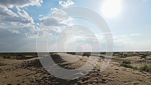 Aerial view from a drone. Woman in a long leopard dress walks along a high dune in the desert with grass in summer in