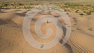 Aerial view from a drone. Woman in a long leopard dress walks along a high dune in the desert with grass in summer in