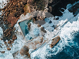 Aerial view early morning light with ocean waves flowing over rocks around North Curl Curl ocean rock pool during storm.