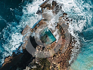 Aerial view early morning light with ocean waves flowing over rocks around North Curl Curl ocean rock pool during storm.