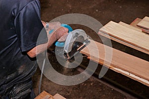 Aerial view of electric circular saw is being cut a piece of wood against hands of senior carpenter in carpentry workshop.