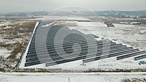 Aerial view of electrical power plant with solar panels covered with snow melting down in winter end for producing clean