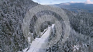 Aerial view of empty snowy road in winter forest in unmaintained mountain pass.