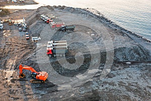 Aerial view of excavator and dump trucks during earthworks on construction site by the sea side. Construction industry