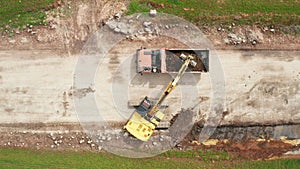 Aerial view of excavator loading a dump truck with soil in the green field