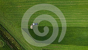 Aerial view of farming tractor mowing green field.