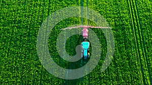 Aerial view of farming tractor plowing and spraying on green field