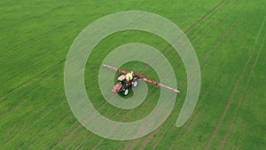 Aerial view of farming tractor plowing and spraying green wheat field. Protection of crop with applying of pesticides
