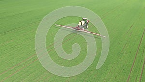 Aerial view of farming tractor plowing and spraying green wheat field. Protection of crop with applying of pesticides