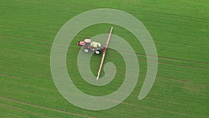 Aerial view of farming tractor plowing and spraying green wheat field. Protection of crop with applying of pesticides