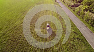 Aerial view of farming tractor spraying on field with sprayer, herbicides and pesticides at sunset. Farm machinery