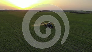 Aerial view of farming tractor spraying on field with sprayer, herbicides and pesticides at sunset. Farm machinery