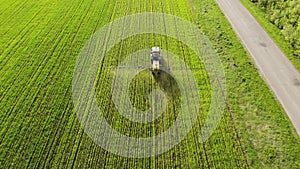 Aerial view of farming tractor spraying on field with sprayer, herbicides and pesticides at sunset. Farm machinery