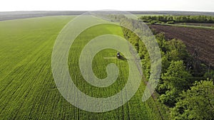 Aerial view of farming tractor spraying on field with sprayer, herbicides and pesticides at sunset. Farm machinery