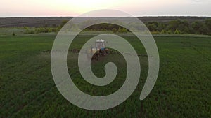 Aerial view of farming tractor spraying on field with sprayer, herbicides and pesticides at sunset. Farm machinery