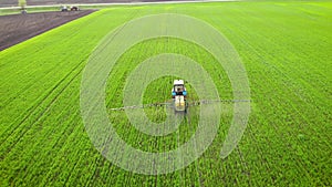 Aerial view of farming tractor spraying on field with sprayer, herbicides and pesticides at sunset. Farm machinery