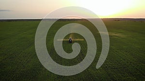 Aerial view of farming tractor spraying on field with sprayer, herbicides and pesticides at sunset. Farm machinery