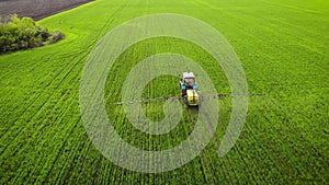 Aerial view of farming tractor spraying on field with sprayer, herbicides and pesticides at sunset. Farm machinery