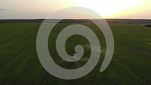 Aerial view of farming tractor spraying on field with sprayer, herbicides and pesticides at sunset. Farm machinery