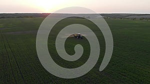 Aerial view of farming tractor spraying on field with sprayer, herbicides and pesticides at sunset. Farm machinery