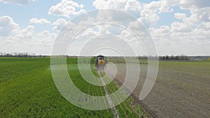 Aerial view of farming tractor spraying on field with sprayer, herbicides and pesticides at sunset. Farm machinery