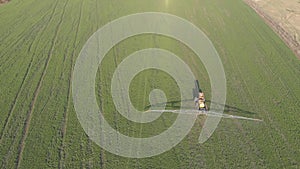 Aerial view of farming tractor spraying on field with sprayer, herbicides and pesticides at sunset. Farm machinery