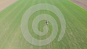 Aerial view of farming tractor spraying on field with sprayer, herbicides and pesticides at sunset. Farm machinery