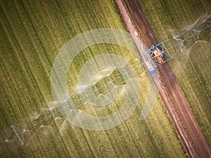 Aerial view of farming tractor spraying on field with sprayer, herbicides and pesticides at sunset. Farm machinery