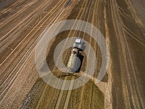 Aerial view of a farming tractor with a trailer fertilizes a freshly plowed agriculural field with manure