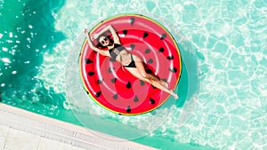 Aerial view of female in bikini lying on a floating inflatable mattress watermelon in swimming pool water. Above view