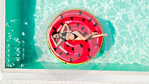 Aerial view of female in bikini lying on a floating inflatable mattress watermelon in swimming pool water. Above view