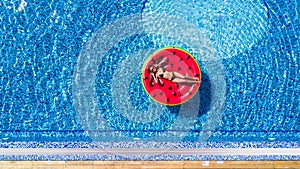 Aerial view of female in bikini lying on a floating mattress in swimming pool. Summer vacation concept