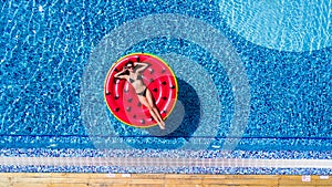 Aerial view of female in bikini lying on a floating mattress in swimming pool. Summer vacation concept