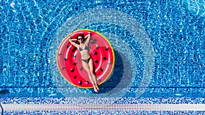 Aerial view of female in bikini lying on a floating mattress in swimming pool. Summer vacation concept