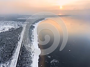 Aerial view at the Finland gulf with the Baltic sea, road passing along seaside. Winter season with snowy trees and sandy beach,